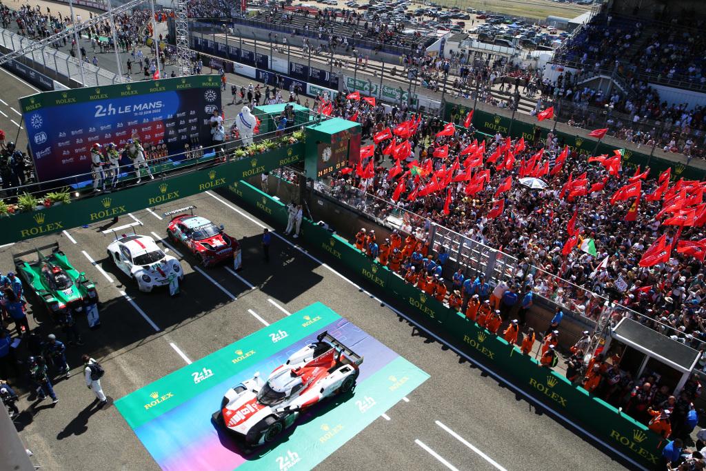 Fans celebrating on track as the winners of the 2022 24 Hours of Le Mans spray champagne on the podium